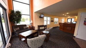Eine Hotellobby mit einer Couch, Sesseln, einem Couchtisch, einem Fernseher und einer Rezeption.
