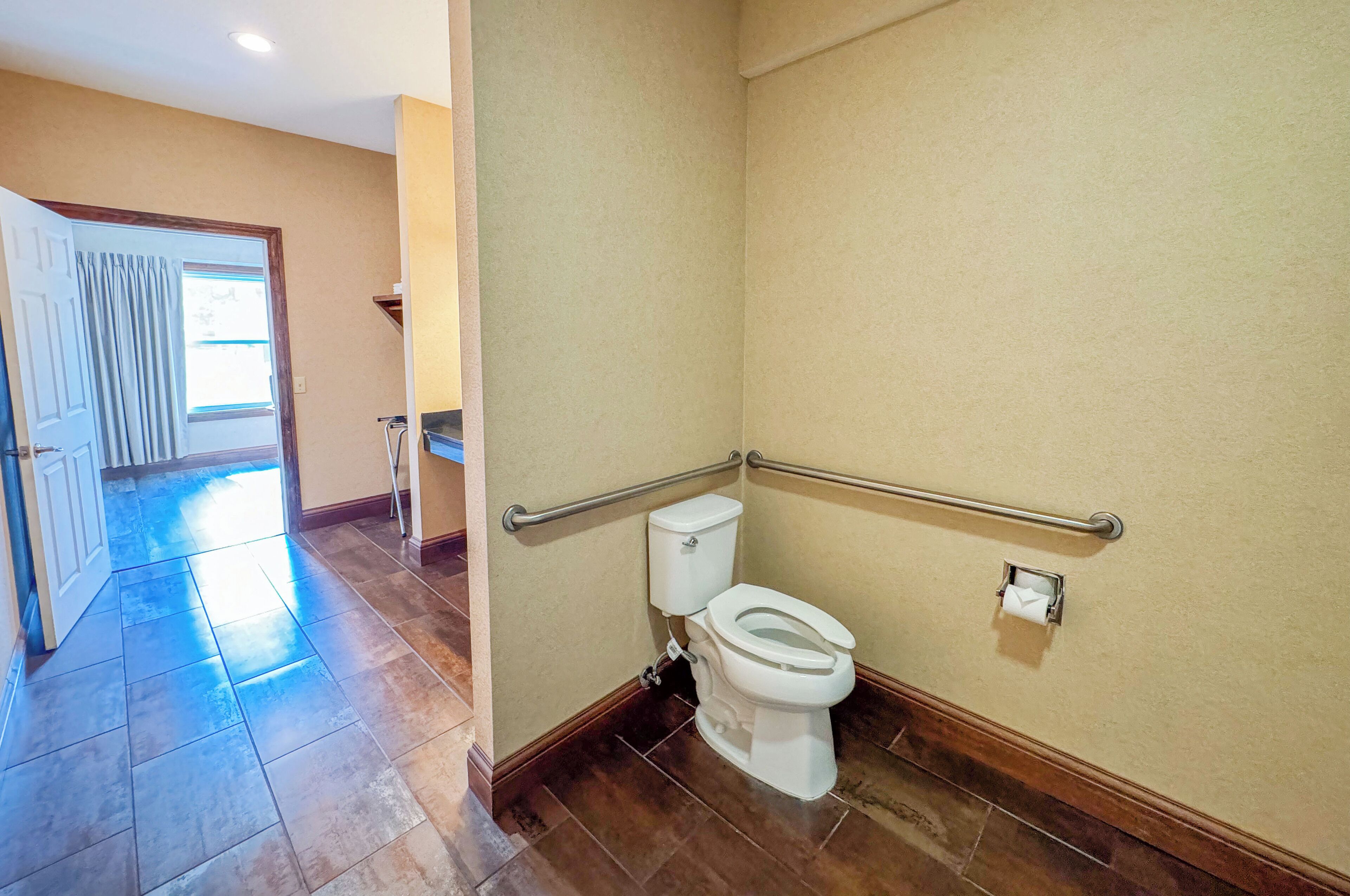 Baño con inodoro, barandilla y dispensador de toallas.