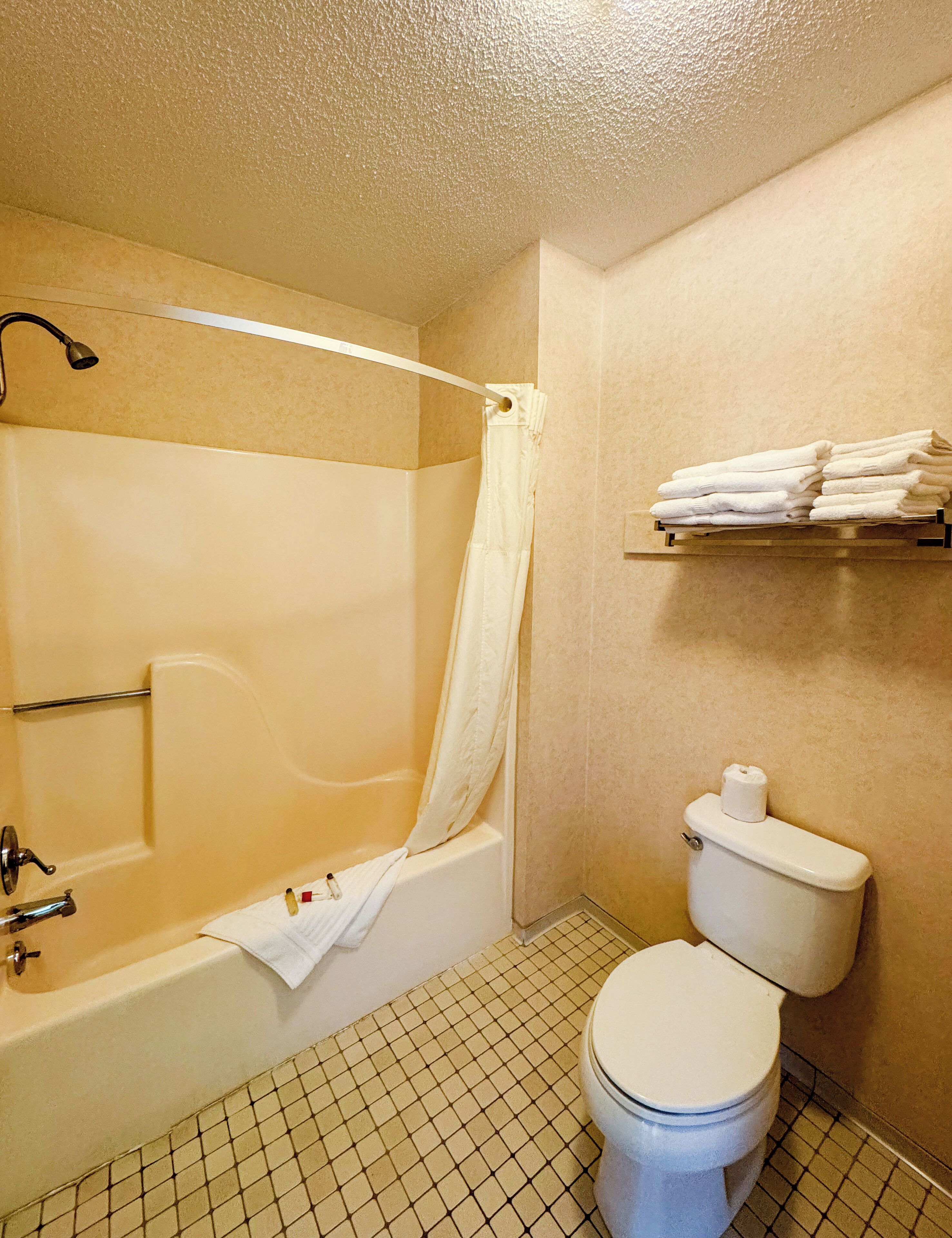 A bathroom with a bathtub, toilet, and a shelf with towels.