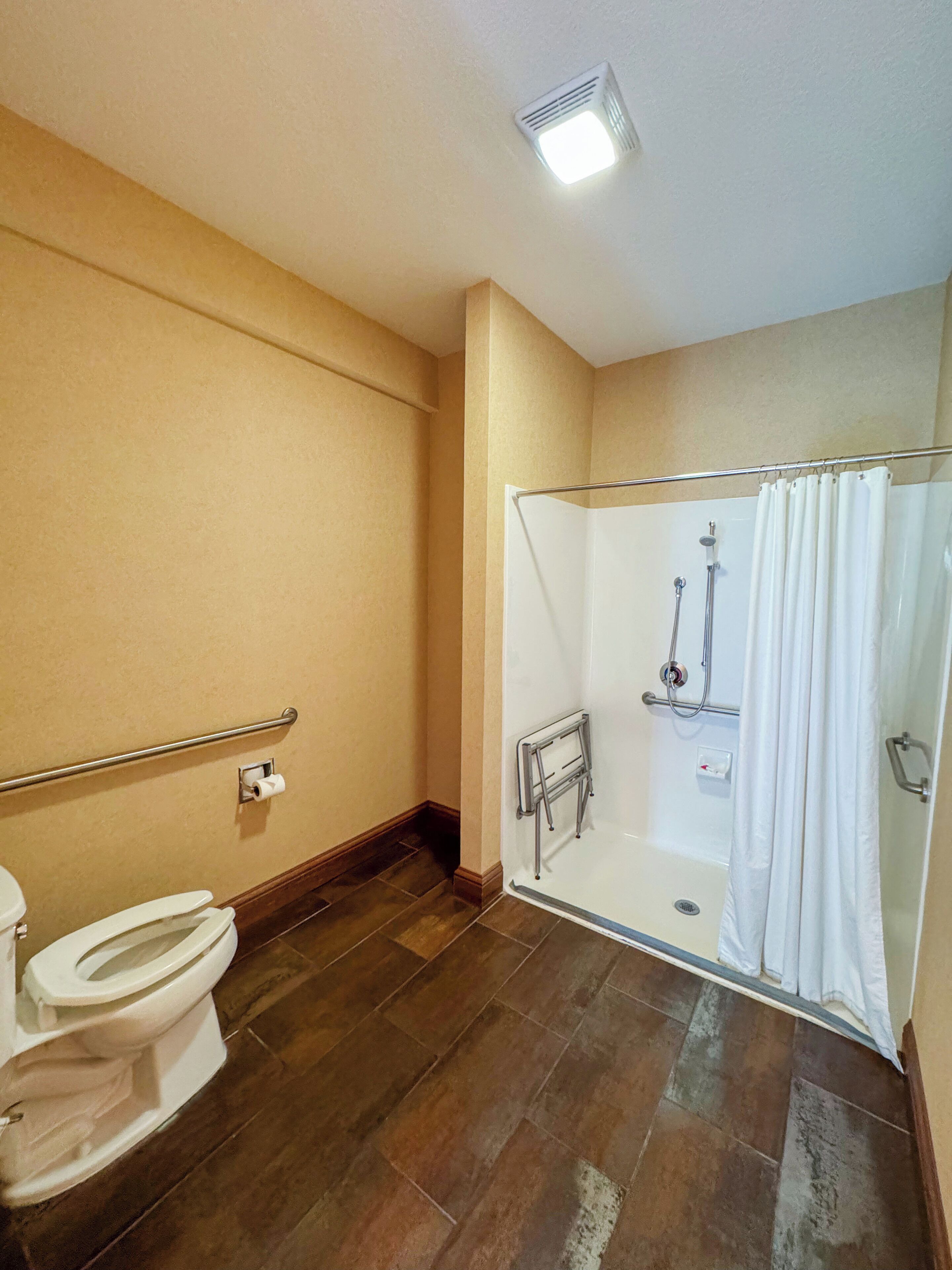 Un baño con inodoro, ducha con puerta de cristal y barandilla.