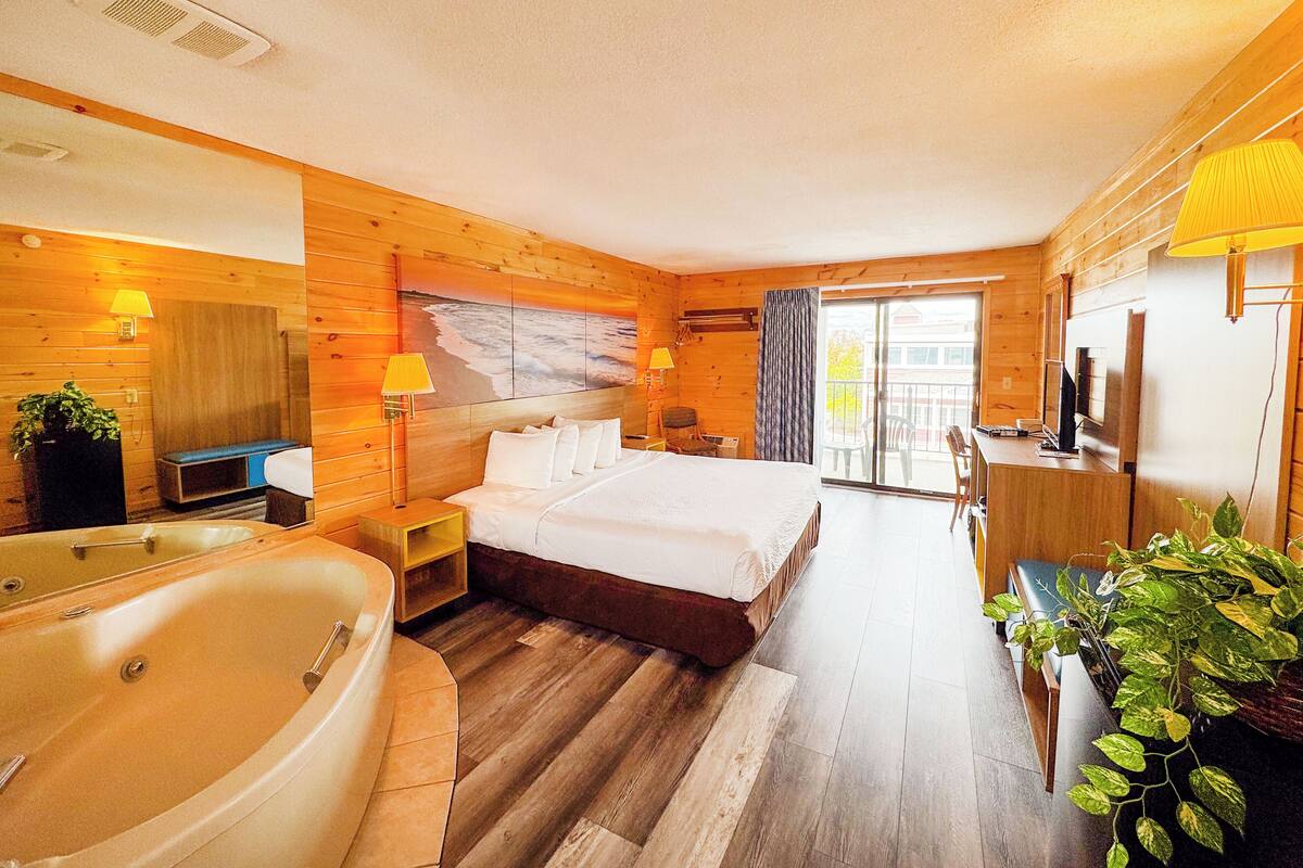 Ein Hotelzimmer mit einem großen Bett, einer Badewanne, einem Schreibtisch mit Computer sowie einem Balkon mit Stühlen.