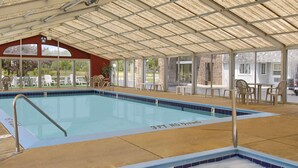 Ein überdachter Innenpool mit klarem, blauen Wasser, eine Terrasse mit Stühlen und Tischen.
