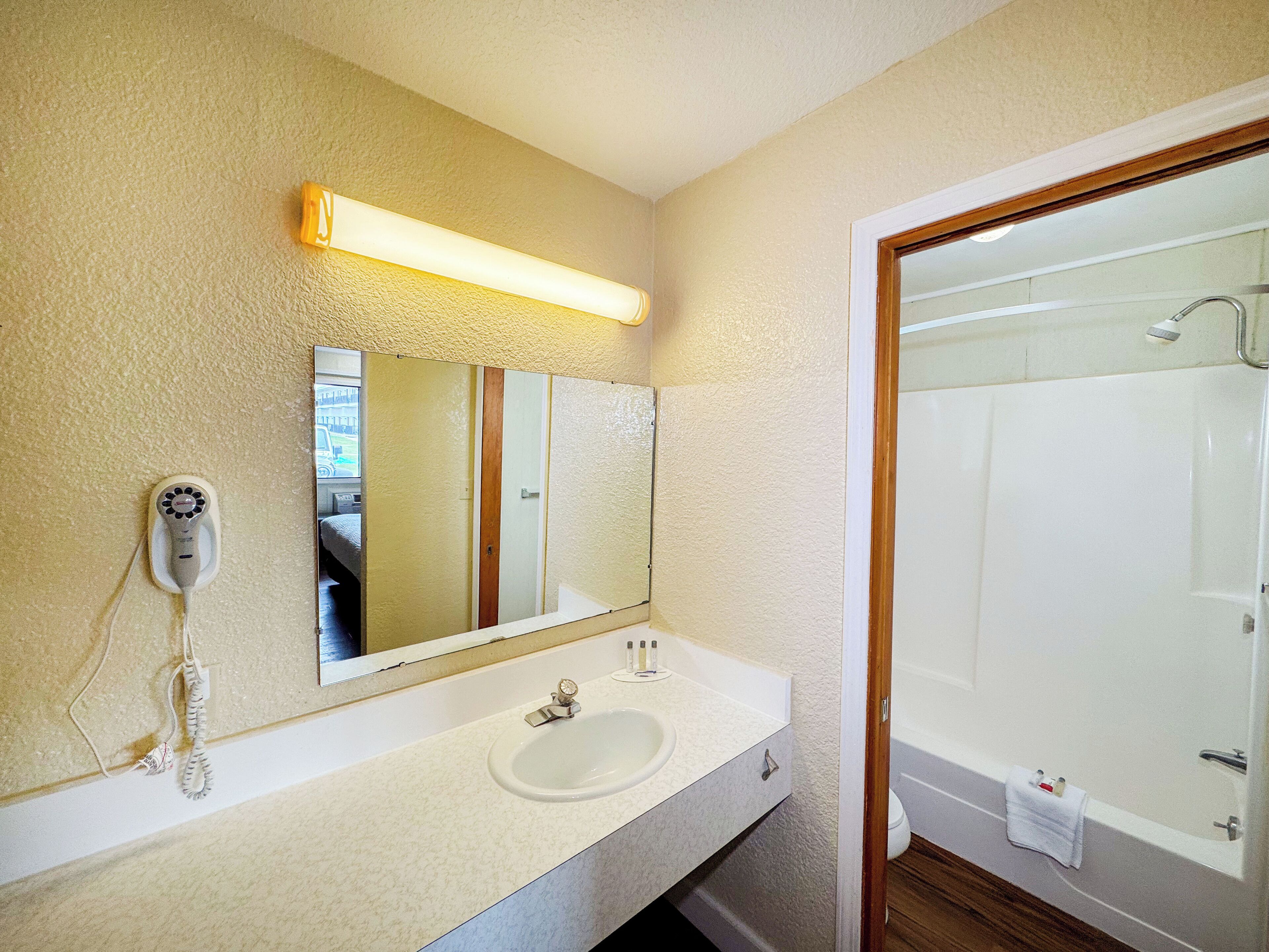 A bathroom with a large mirror, a sink, a hairdryer, and a shower.