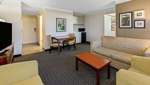 A hotel room with a living area, a dining table with chairs, a sofa, a television, and a kitchenette.