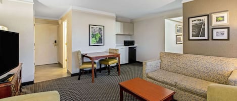 Hotelkamer met een zithoek, een eettafel met stoelen, een bank, een televisie en een kitchenette.