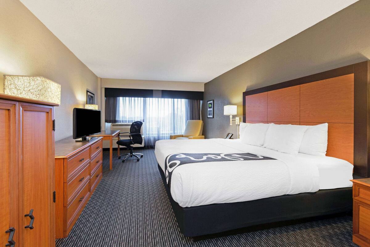Une chambre d’hôtel avec un grand lit, un bureau avec un ordinateur, une télévision et une armoire.