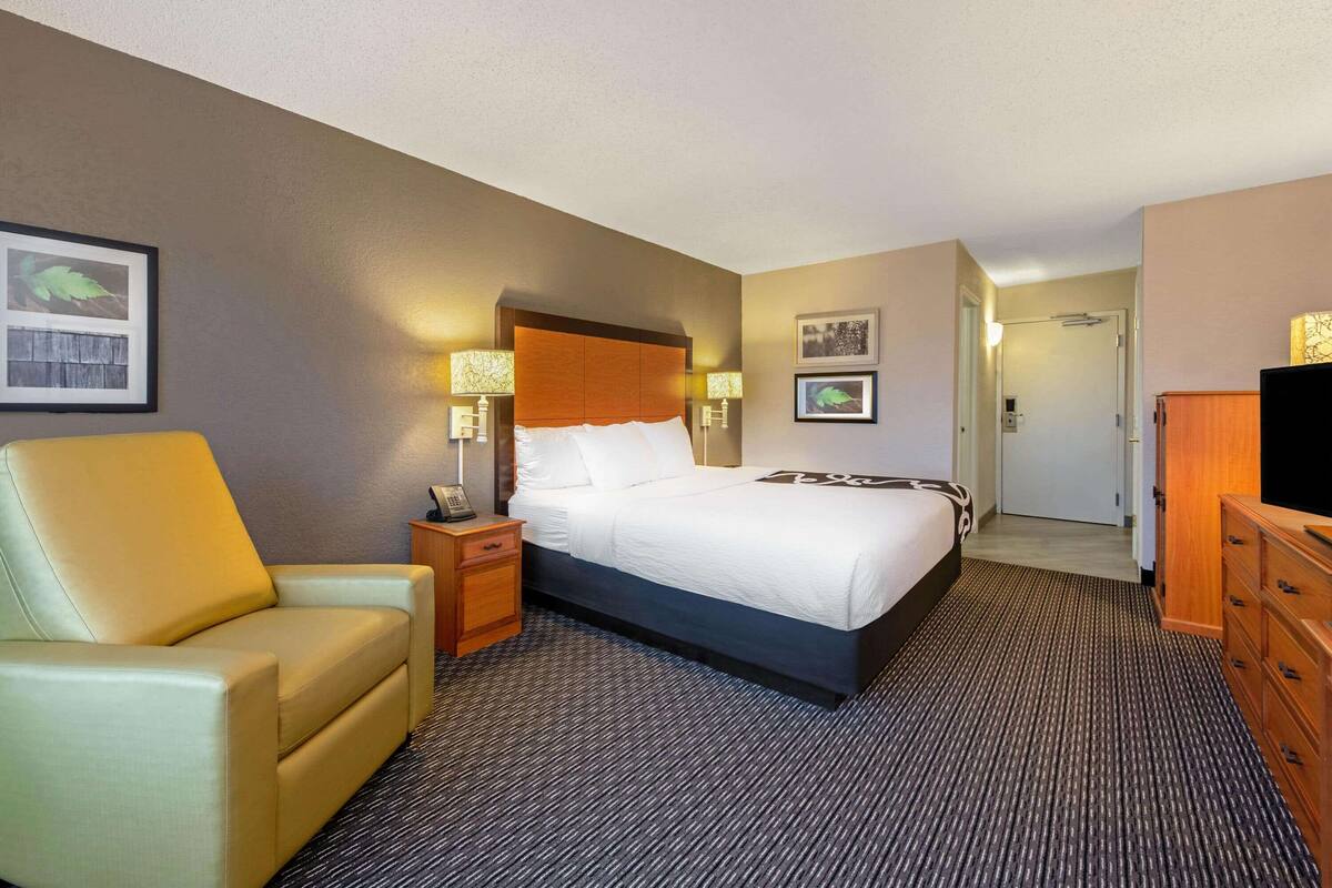 Une chambre d’hôtel comprenant un lit, une chaise, une table de chevet, une lampe et une commode.