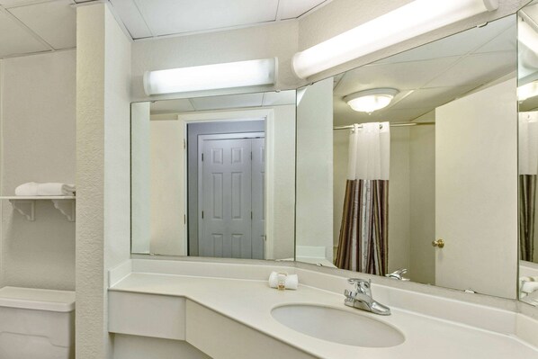A bathroom with a white sink, a mirror, a shower curtain, and a door. - La Quinta Inn & Suites by Wyndham New Orleans Airport (Kenner)
