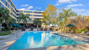 A swimming pool with lounge chairs and umbrellas, surrounded by palm trees and a modern building.