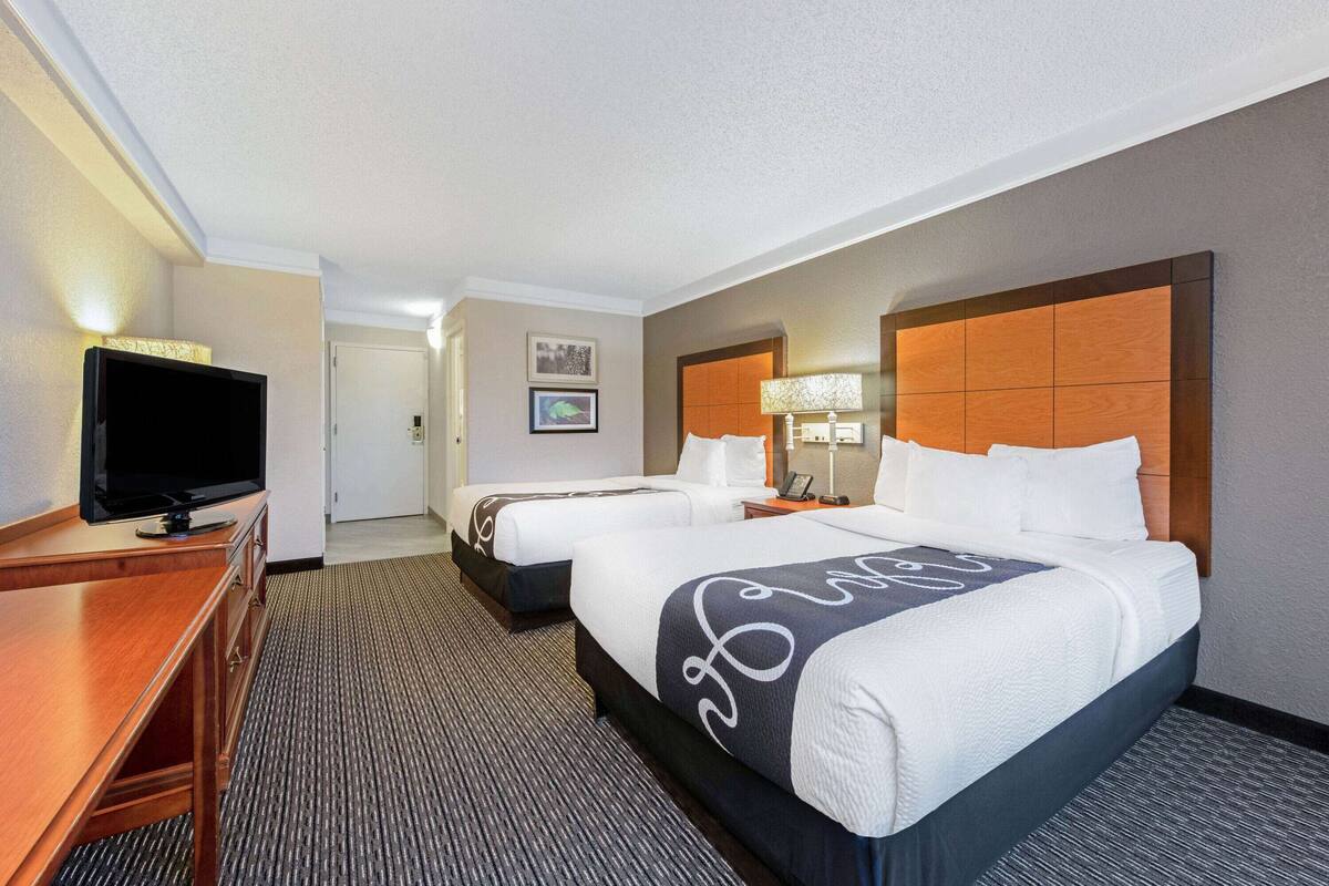 Une chambre d’hôtel avec deux lits, un bureau avec une télévision et une porte donnant sur un couloir.