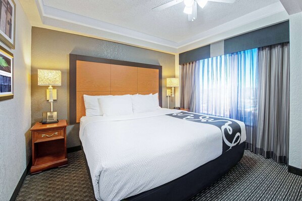 A hotel room with a large bed, two bedside lamps, a nightstand, and a window with curtains. - La Quinta Inn & Suites by Wyndham New Orleans Airport (Kenner)