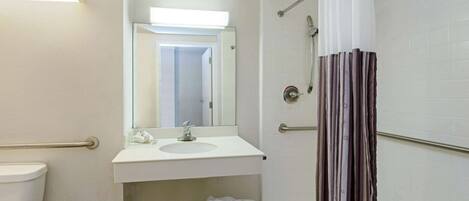 A bathroom with a toilet, sink, mirror, shower, and a towel rack.