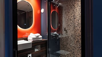 A modern bathroom with a glass shower enclosure, a round mirror, and a vanity with a sink and towel rack.