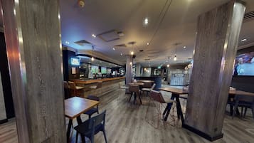 Un restaurante con suelo de madera, mesas, sillas y una zona de bar con un letrero de neón.