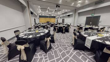 A conference room with multiple round tables, black chairs with beige sashes, and a carpeted floor.