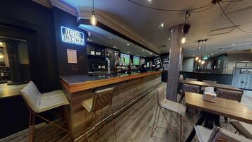 A bar area with a neon sign, wooden bar counter, and metal chairs.