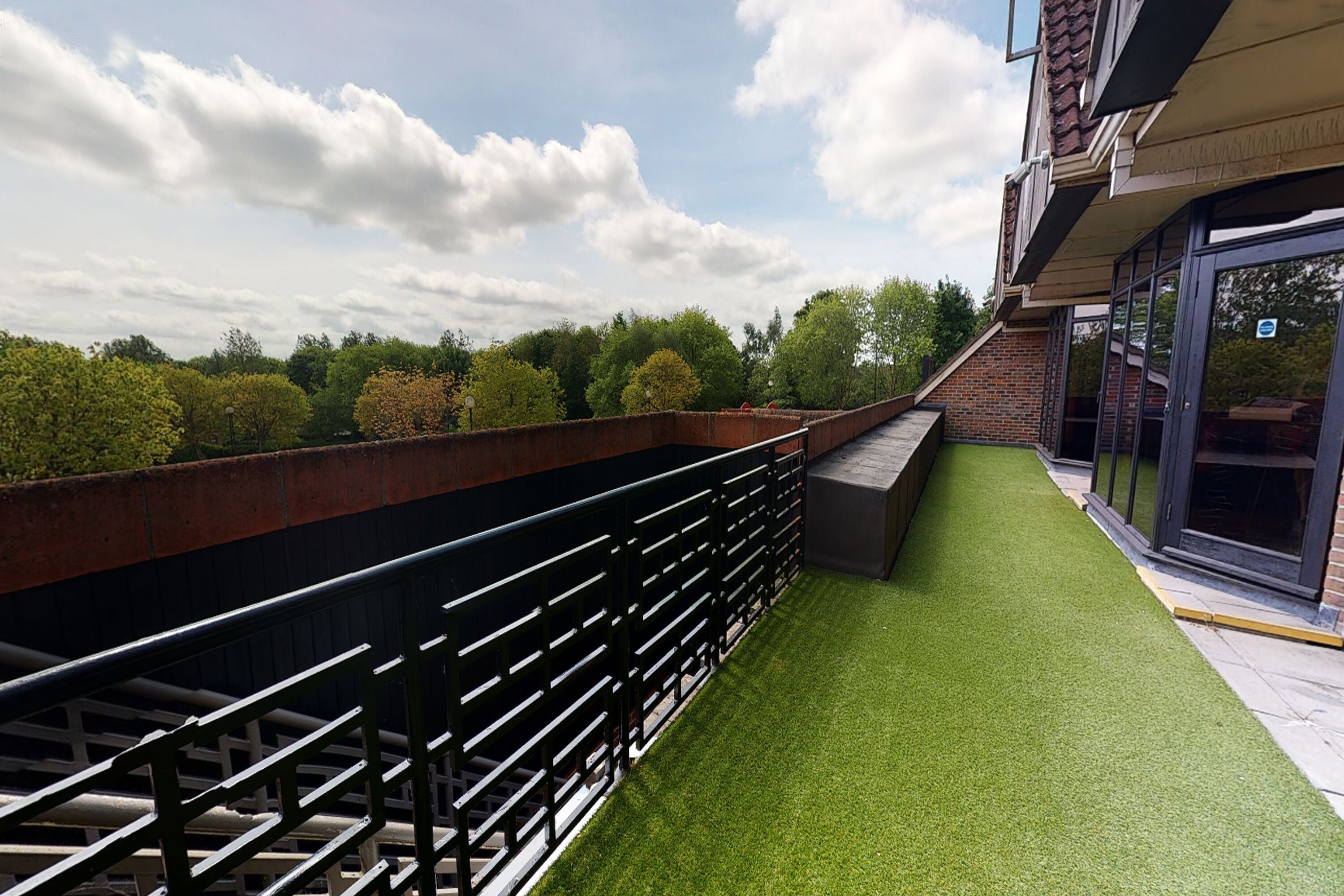 A rooftop terrace with a metal railing, green artificial grass, and a brick wall.