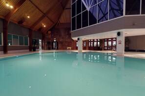 Una piscina interior con techo de madera y amplias ventanas.
