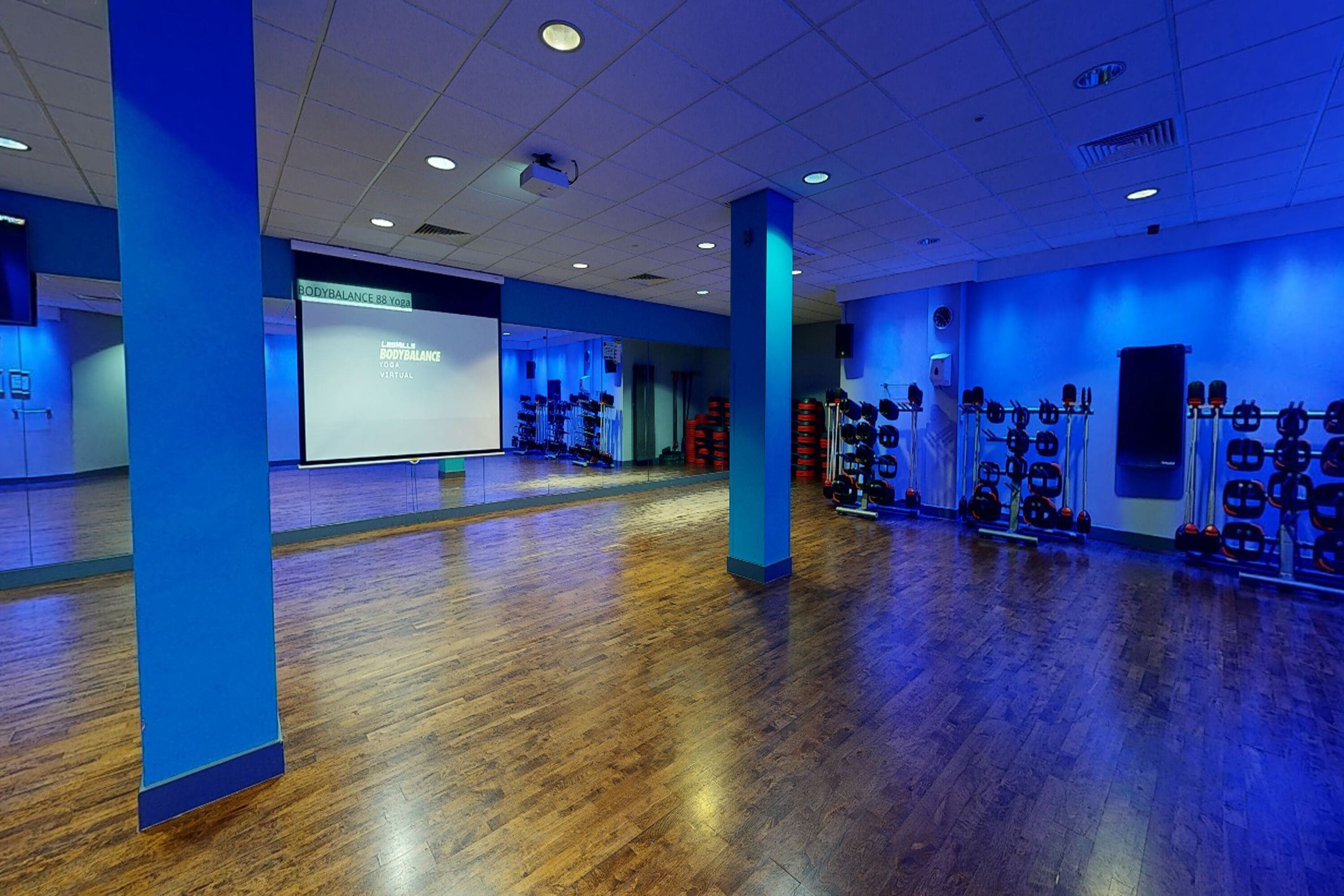 Un gimnasio amplio con pisos de madera, paredes azules y diversos equipos de ejercicio.