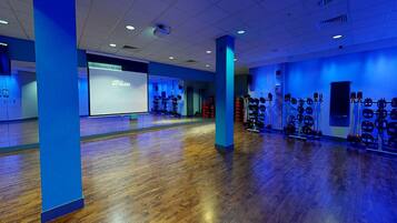 Un gimnasio amplio con pisos de madera, paredes azules y diversos equipos de ejercicio.