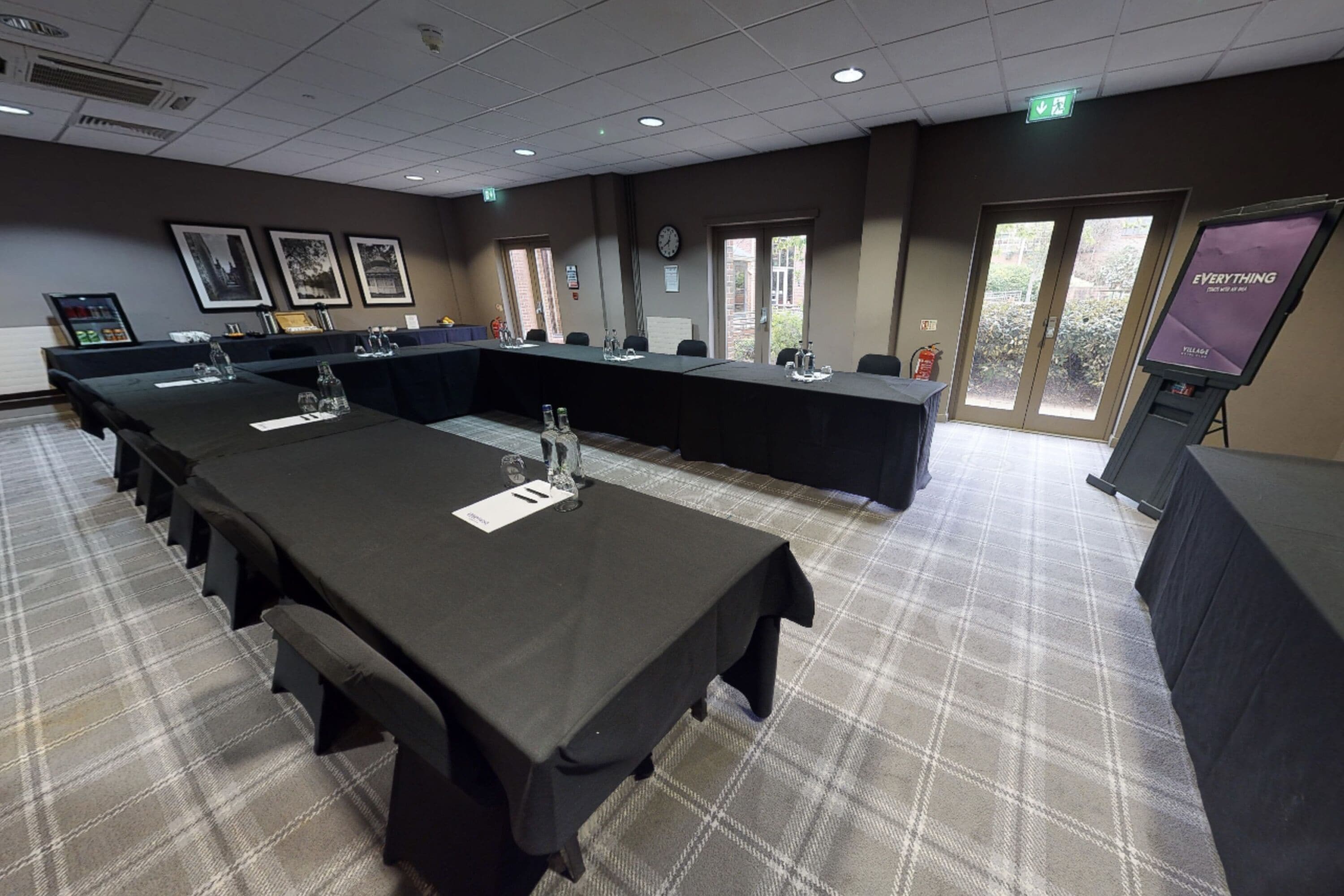 A conference room with a long table, multiple chairs, a clock, framed pictures on the wall, and a screen displaying "EVERYTHING".