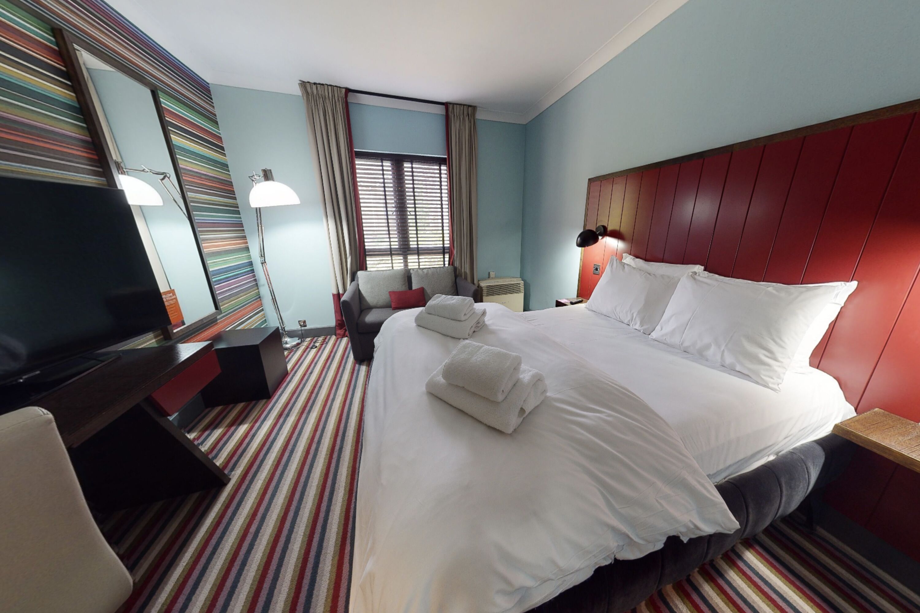 Une chambre d’hôtel avec un grand lit, une télévision, un bureau et une fenêtre avec des rideaux.