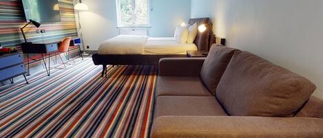 Una habitación de hotel moderna con cama, sofá, escritorio y televisión.