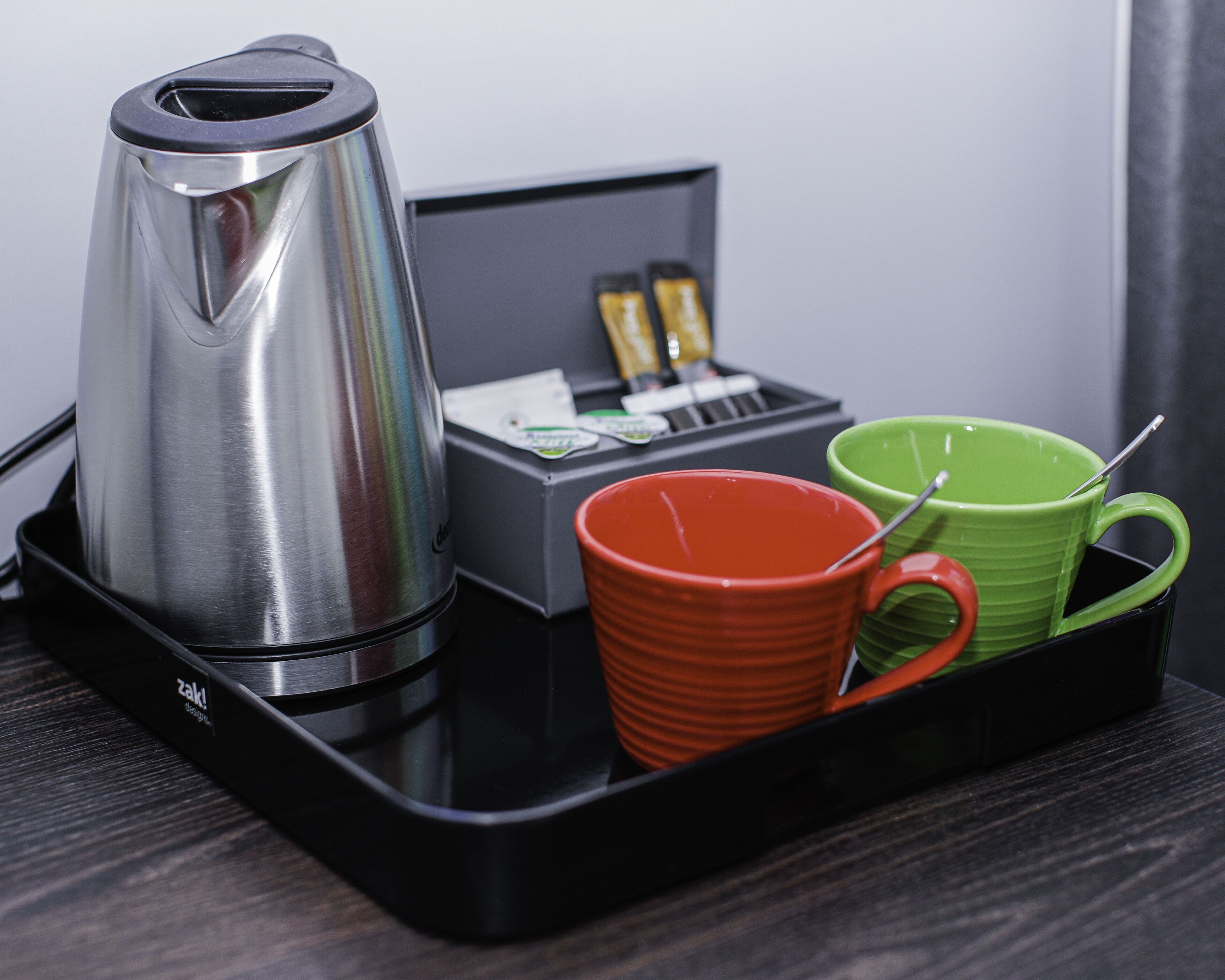 A black tray with a stainless steel coffee maker, a red mug, and a green mug.