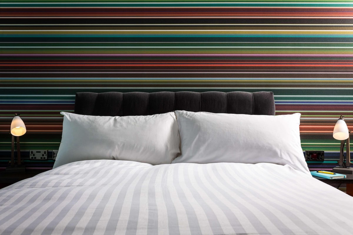 A bed with striped bedding, a headboard with black cushions, and bedside lamps.