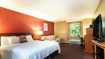 A hotel room with a large bed, a sofa, a television, and a window with curtains.