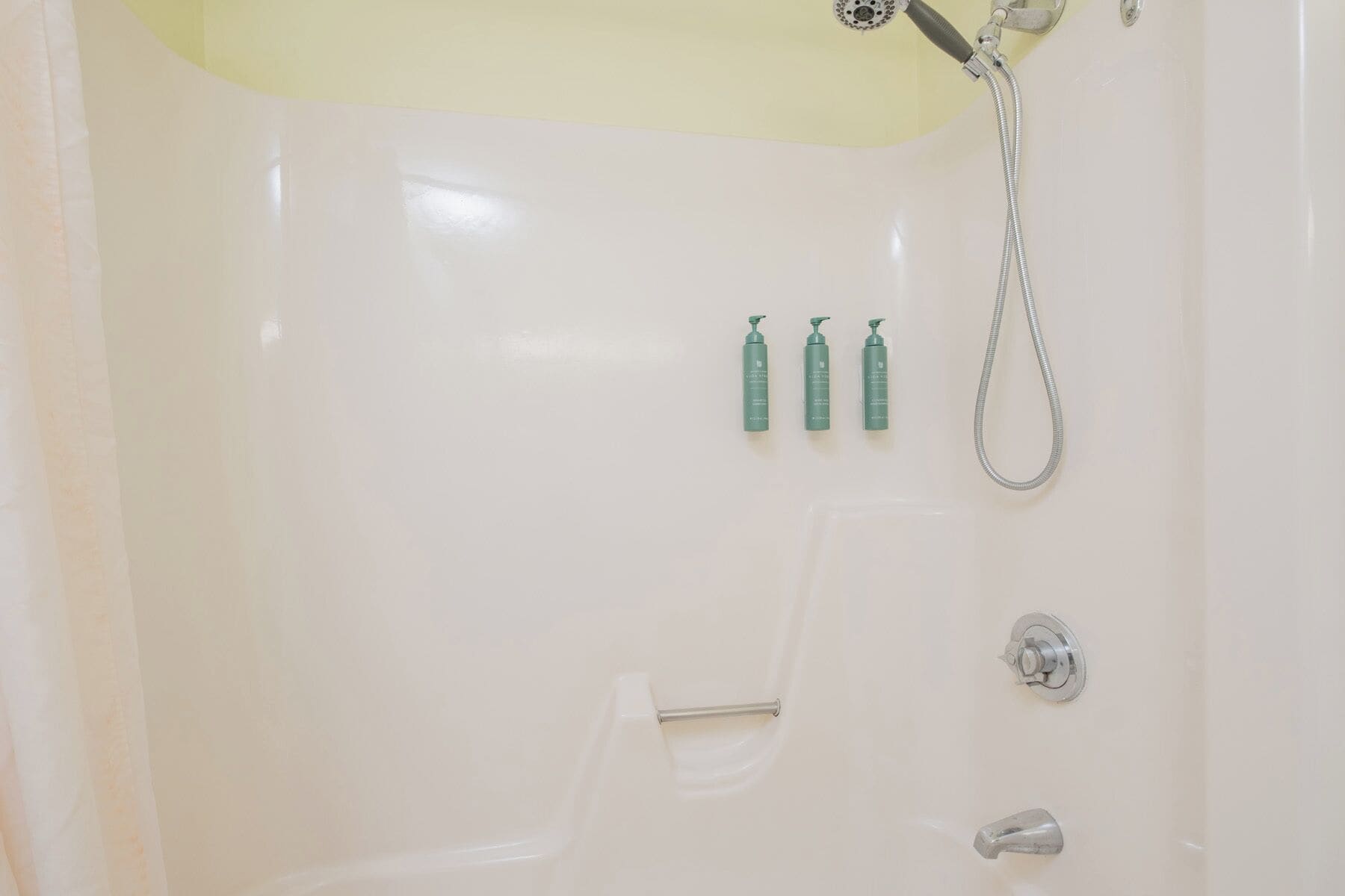 A bathroom with a bathtub, a shower, and three green bottles on the wall.