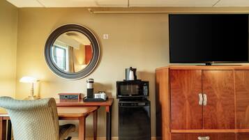 Een hotelkamer met een houten kast, een televisie, een magnetron, een koffiezetapparaat, een bureau met een lamp en een stoel.