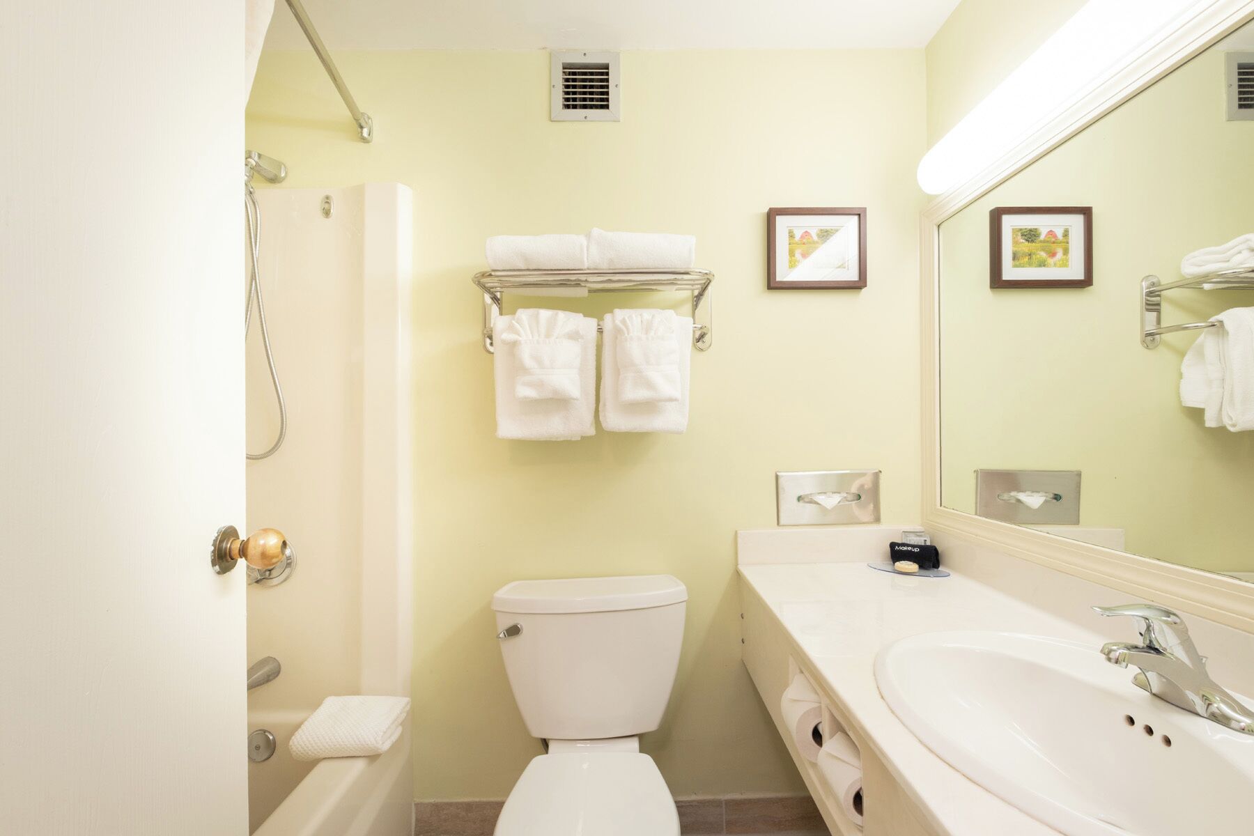 A bathroom with a toilet, sink, and shower. There are towels and a mirror.
