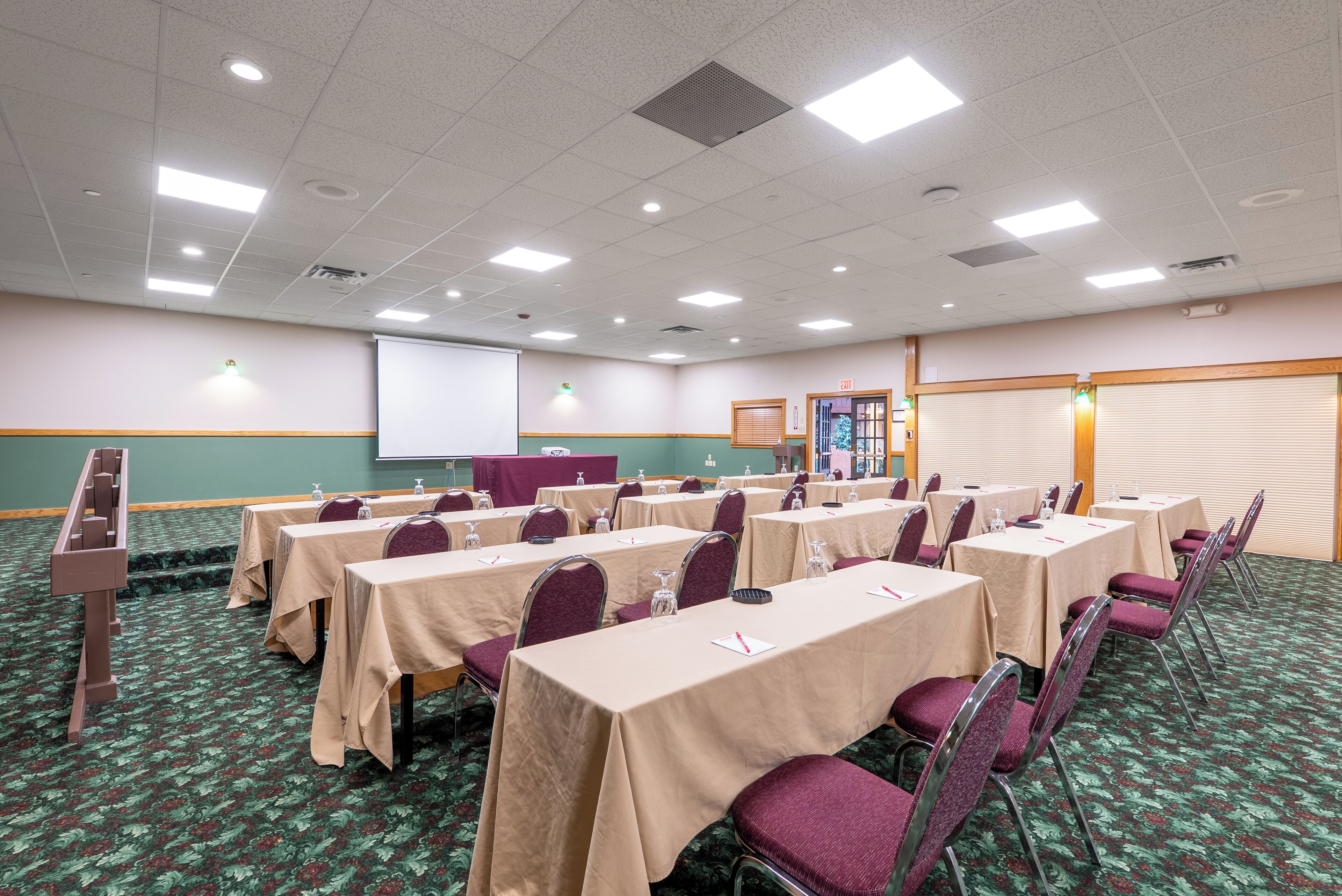 A conference room with tables and chairs, a projector screen, and a carpeted floor.