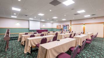 A conference room with tables and chairs, a projector screen, and a carpeted floor.