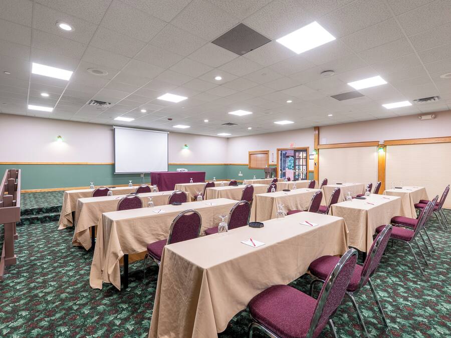 A conference room with tables and chairs, a projector screen, and a carpeted floor.