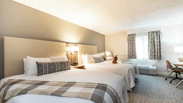 A hotel room with two beds, a desk, a chair, a lamp, and a window with curtains.