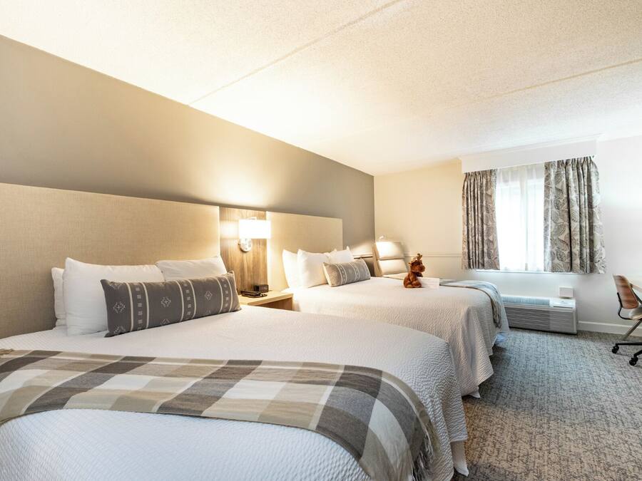 A hotel room with two beds, a desk, a chair, a lamp, and a window with curtains.