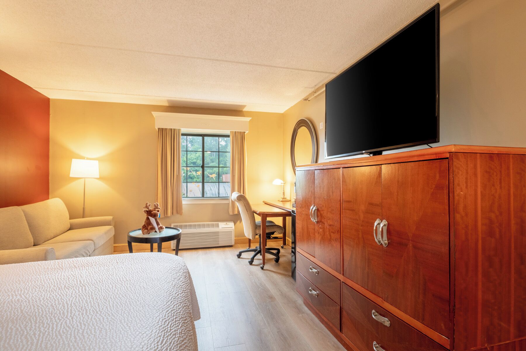 Habitación de hotel con cama, televisión, cómoda de madera, escritorio y silla, y ventana con cortinas.
