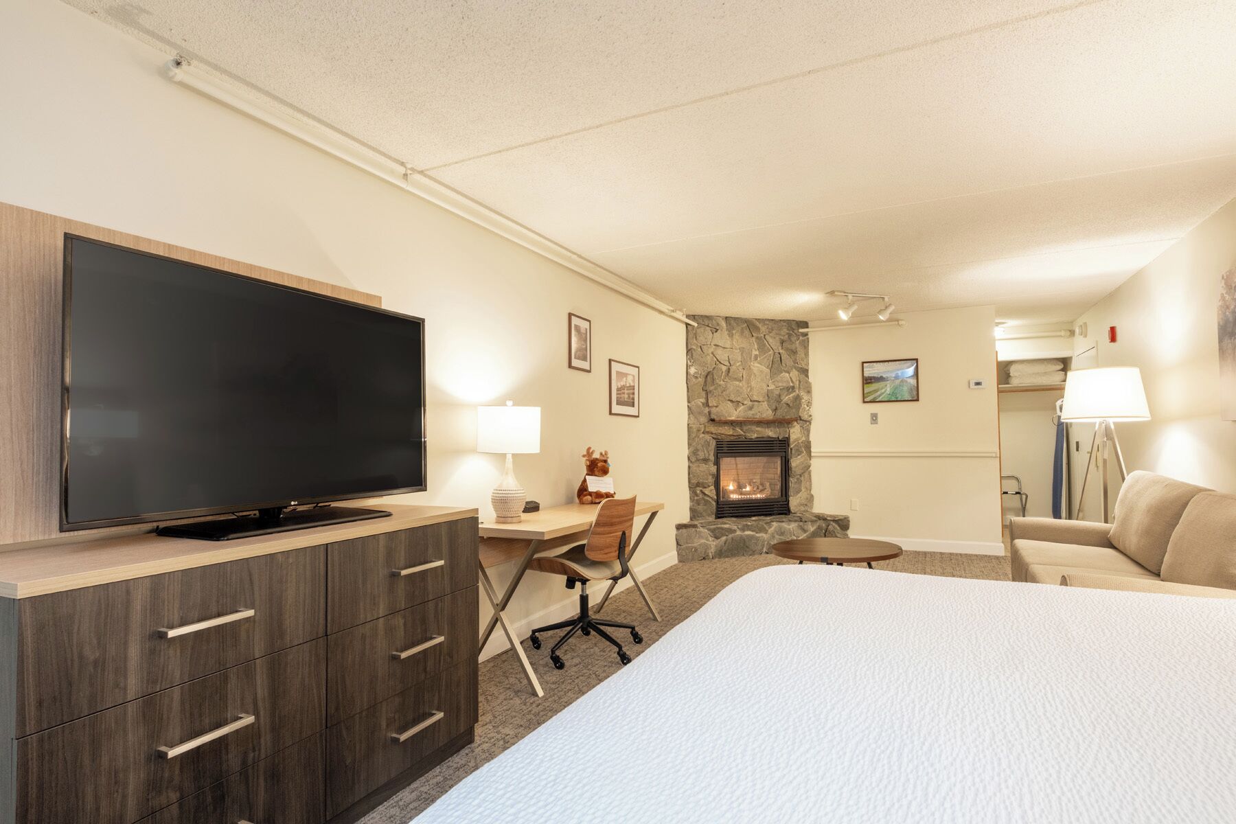 Habitación de hotel con televisión de pantalla plana, chimenea de piedra, cama, escritorio con silla y lámpara.