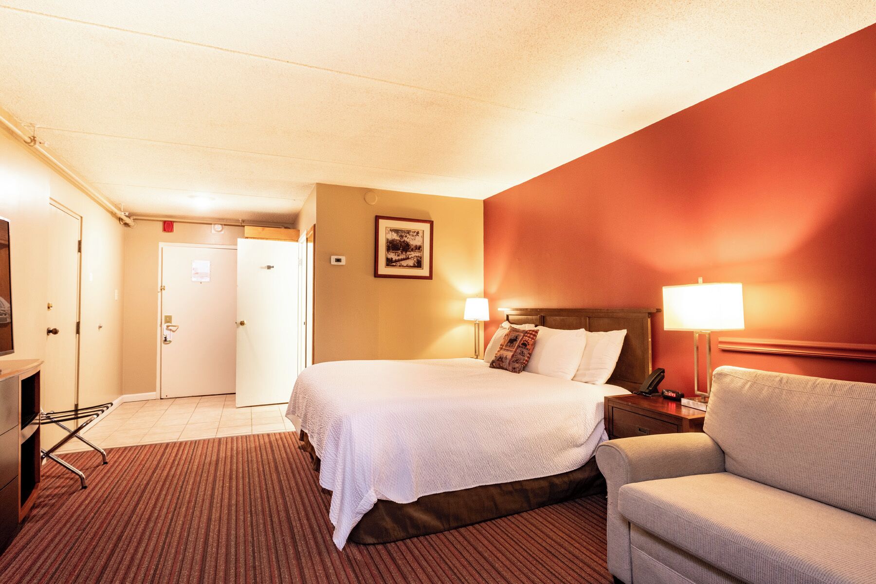 A hotel room with a bed, bedside lamp, chair, and a door leading to a bathroom.