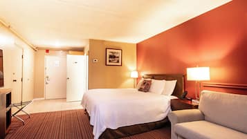 A hotel room with a bed, bedside lamp, chair, and a door leading to a bathroom.