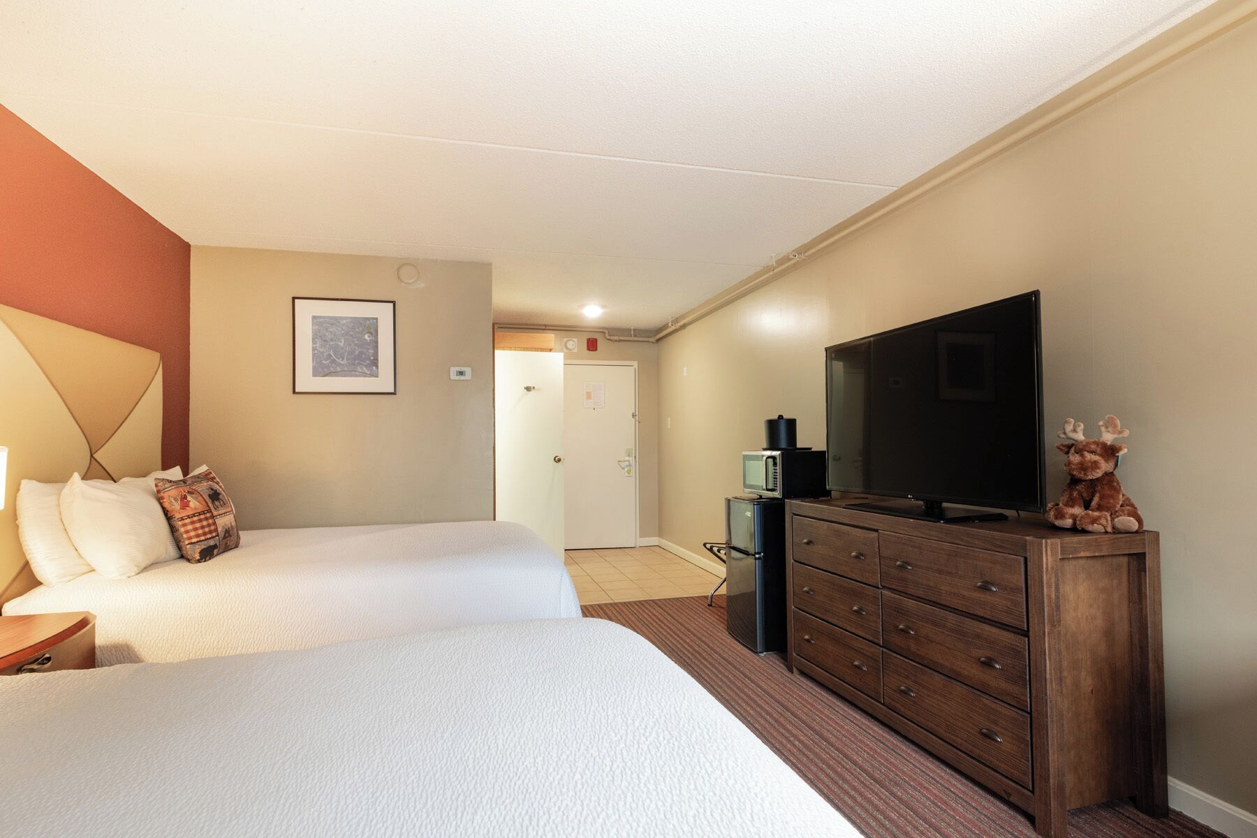 A hotel room with two beds, a dresser, a television, and a microwave.