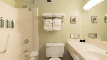Une salle de bain avec une baignoire, des toilettes et un lavabo. Des serviettes sont suspendues sur un porte-serviettes, et un miroir est placé au-dessus du lavabo.