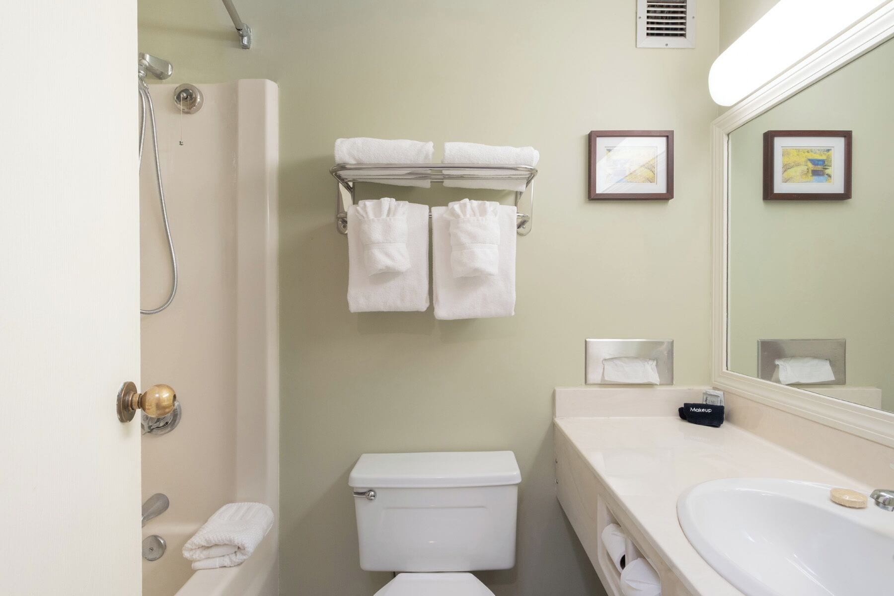 A bathroom with a toilet, sink, and shower. There are towels hanging on a rack and a framed picture on the wall.