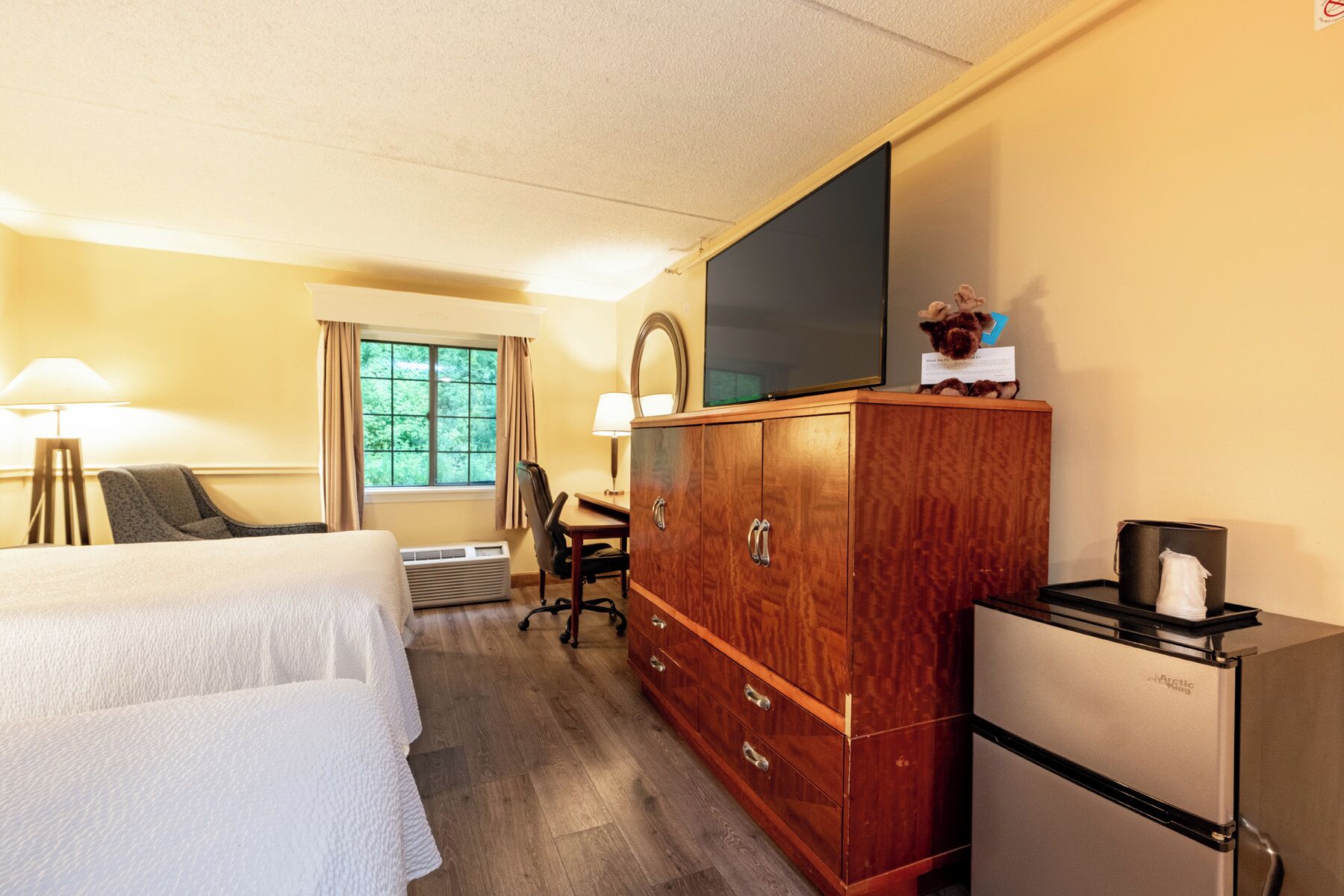 A hotel room with a bed, a desk with a chair, a television, a wardrobe, and a refrigerator.