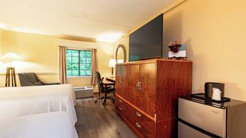 A hotel room with a bed, a desk with a chair, a television, a wardrobe, and a refrigerator.