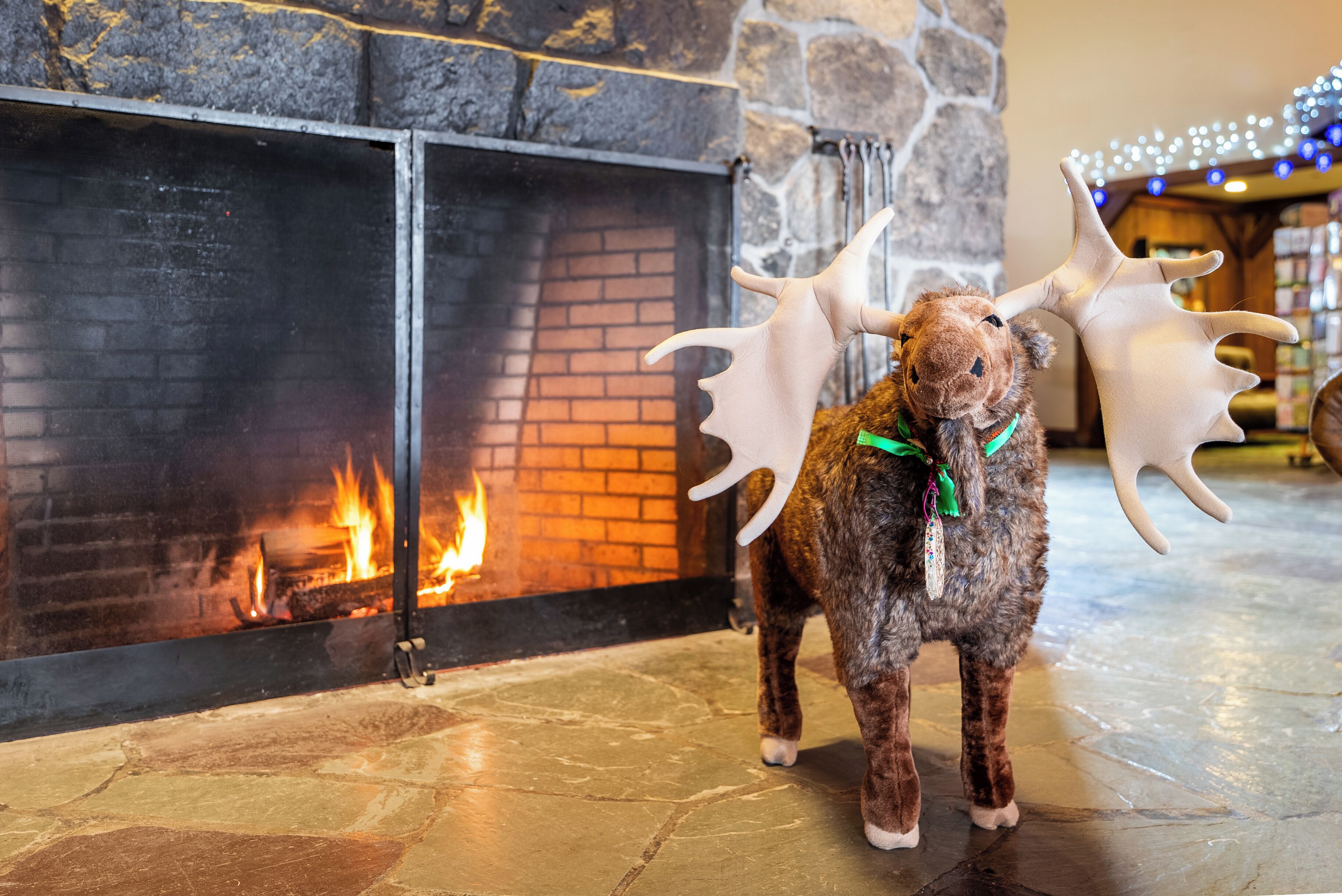 A moose statue with antlers in front of a fireplace with a fire.