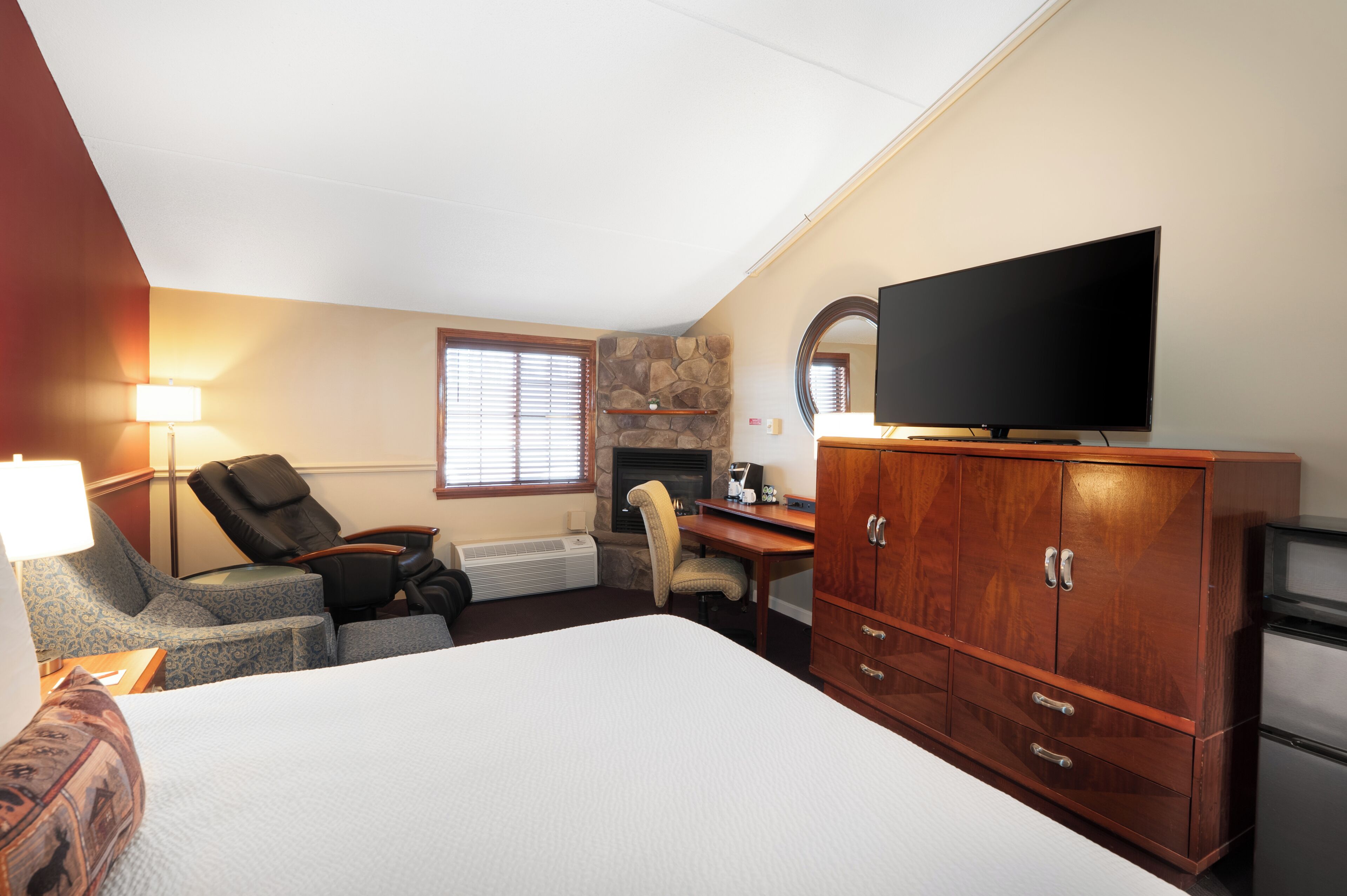 Habitación de hotel con cama, escritorio con silla, televisor, armario, chimenea y ventana con persianas.