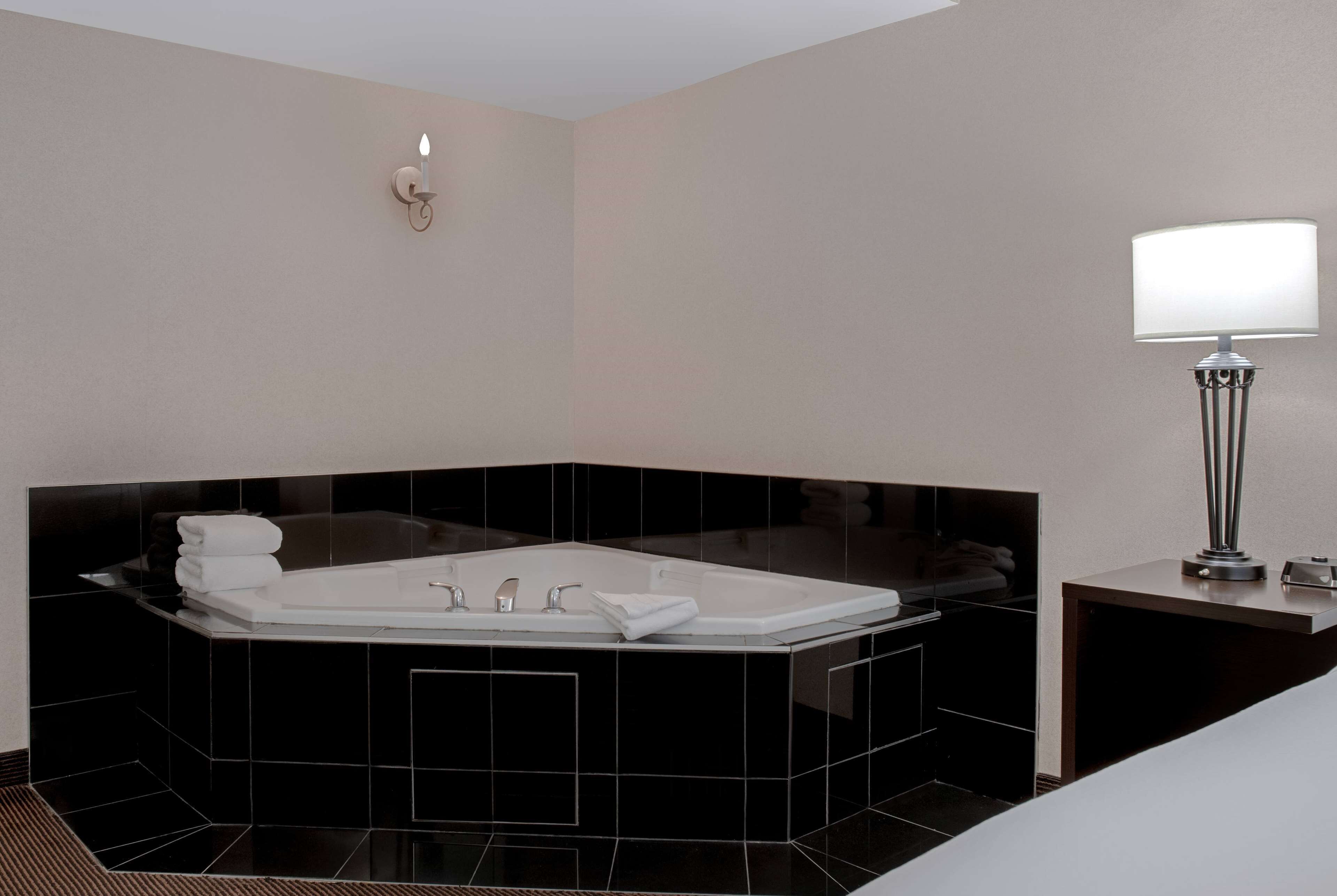 A modern bathroom with a large black bathtub, a white sink, and a wall-mounted light fixture.